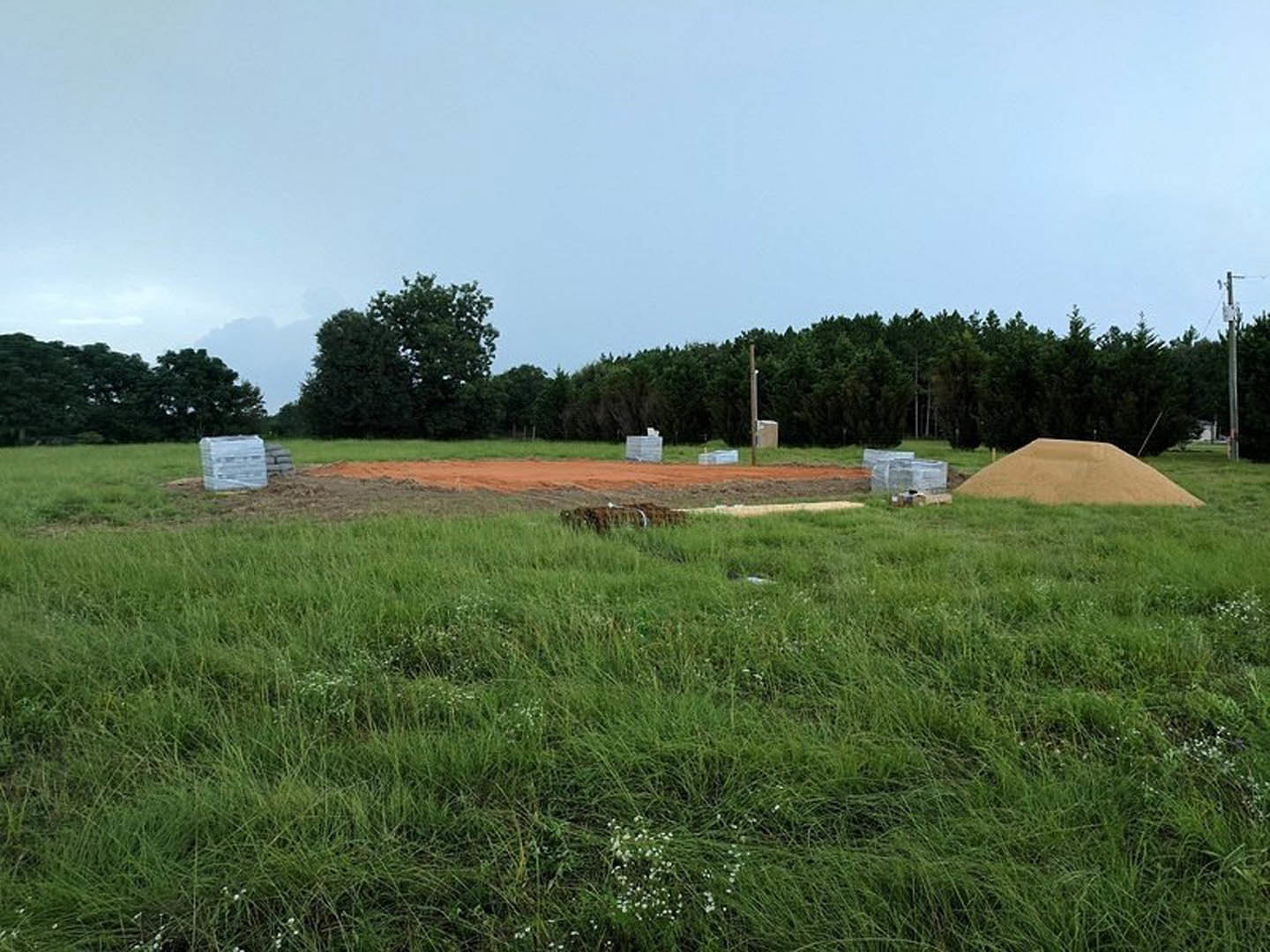 Grassy field with a dirt pit bordered by trees under a clear blue sky