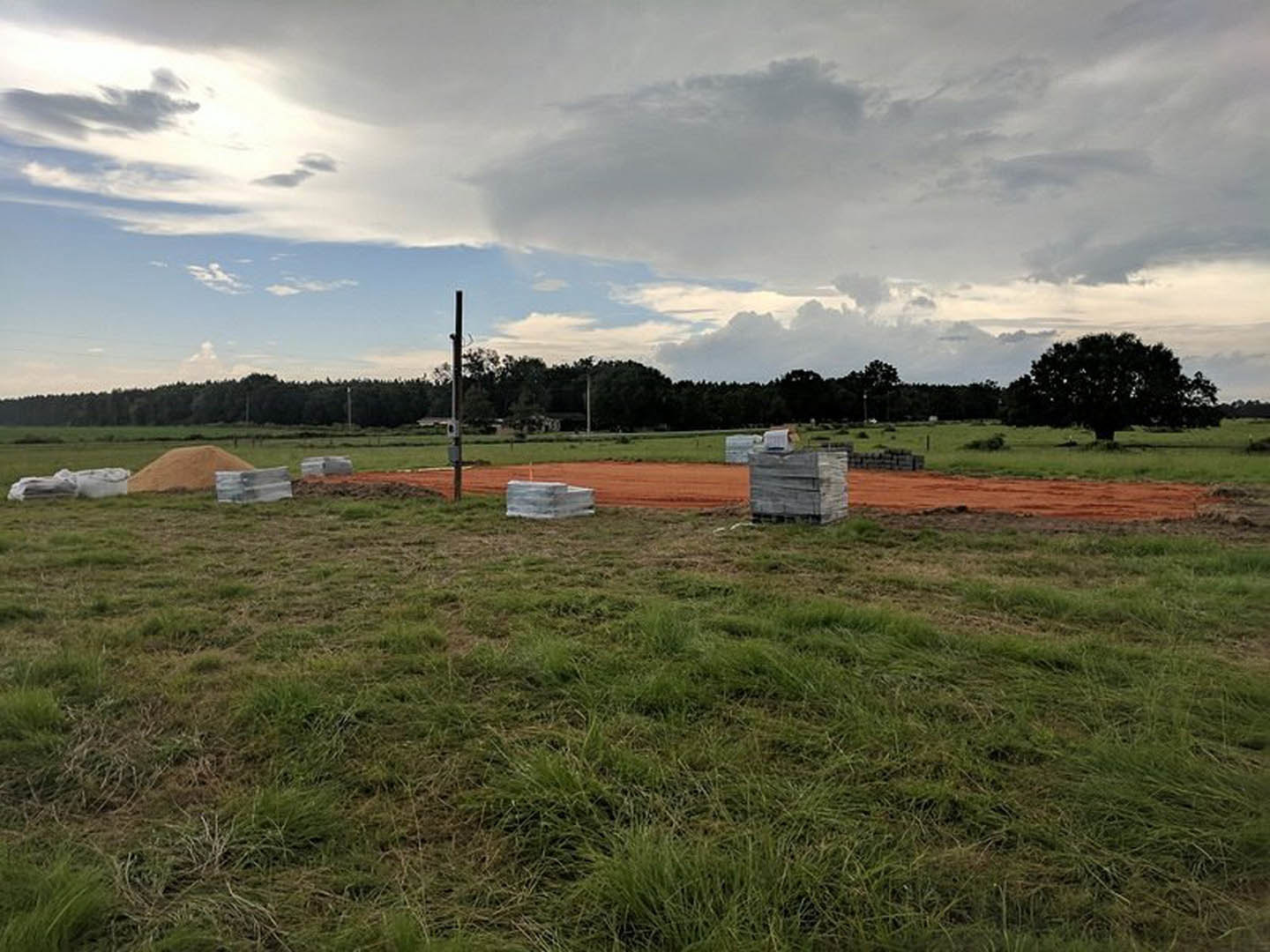 Open field with patches of dirt, cardboard boxes scattered, cloudy sky overhead, trees lining the background