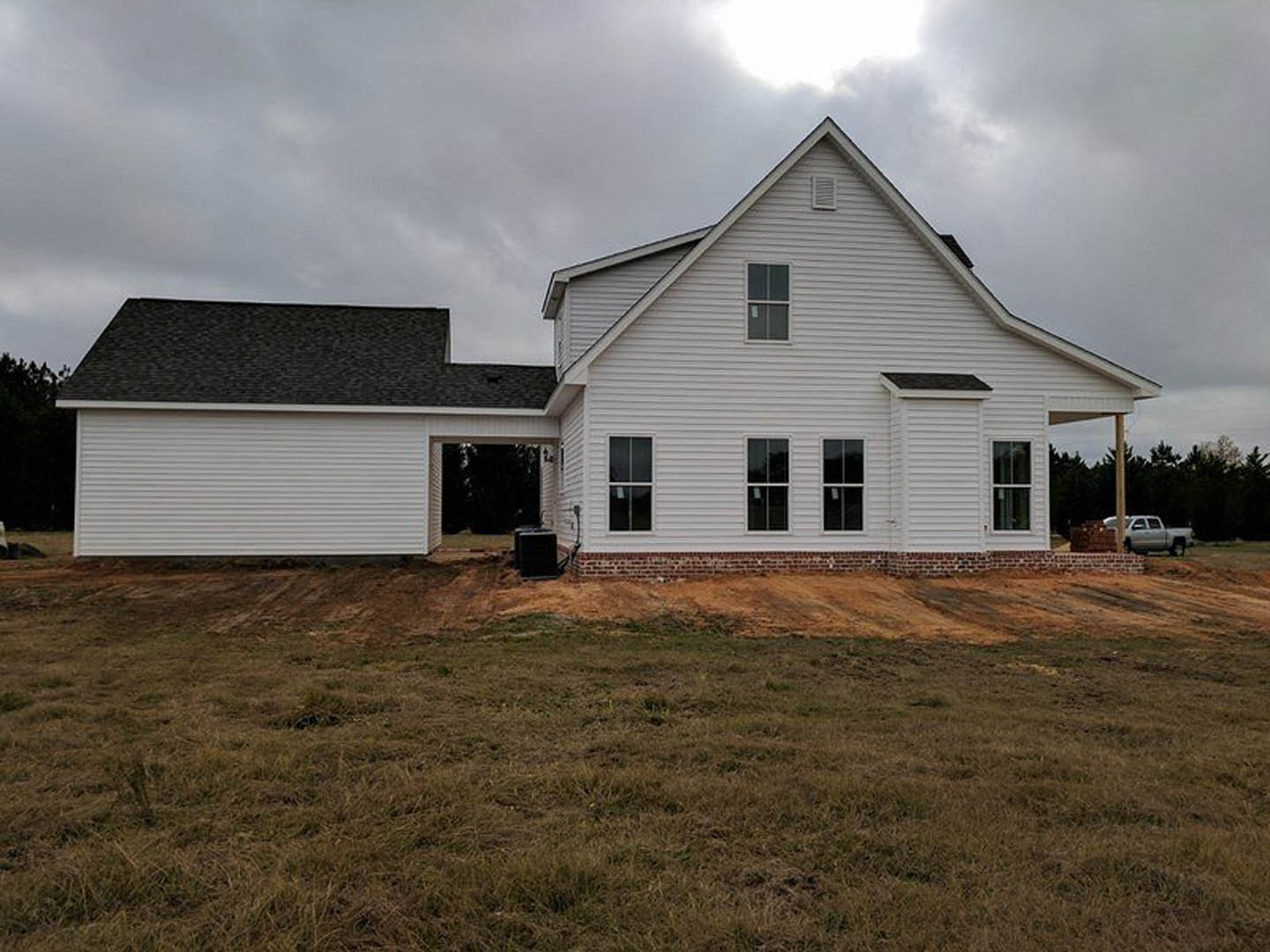 White farmhouse under construction with unfinished roof, grassy field in foreground, cloudy sky overhead, window displaying a sign, black rectangular object near exterior wall