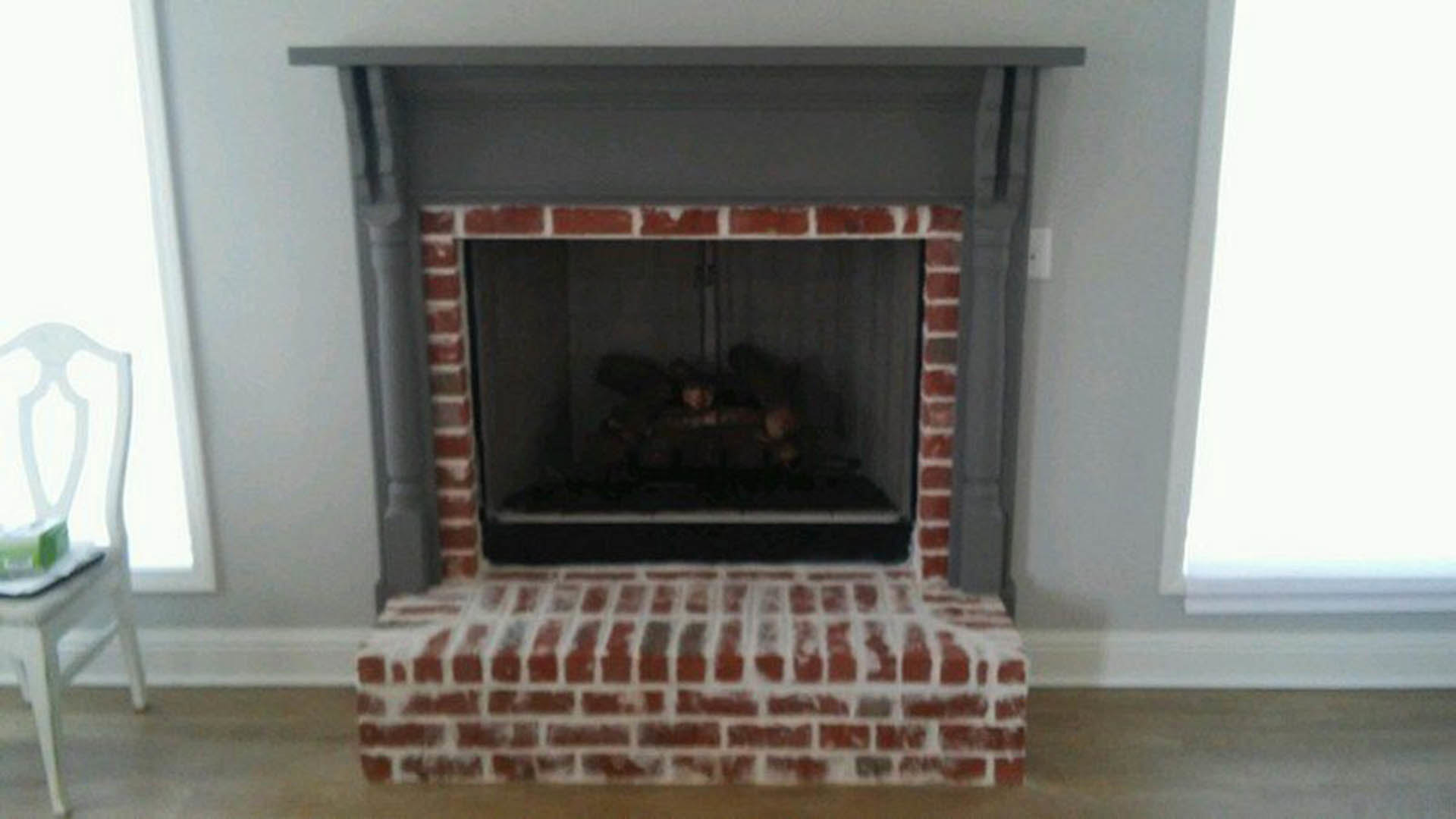 Brick hearth fireplace with black fire screen, white wall, wood shelf, and light-colored floor