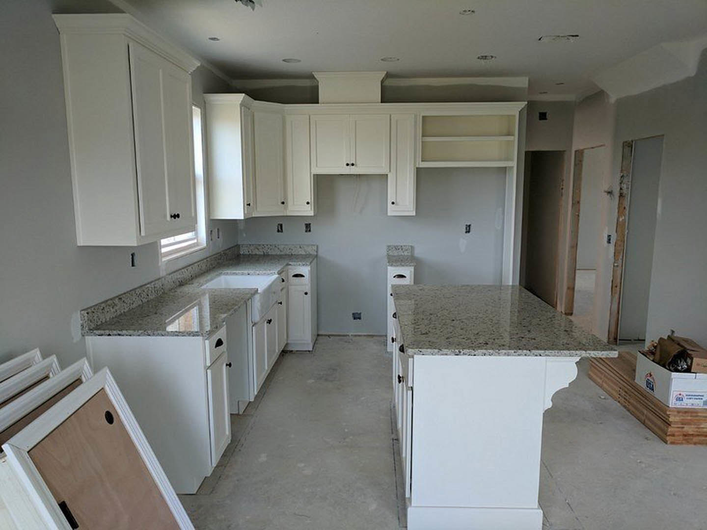 White kitchen with granite countertops, large island with marble top, stainless steel appliances, white cabinetry, and light wood flooring