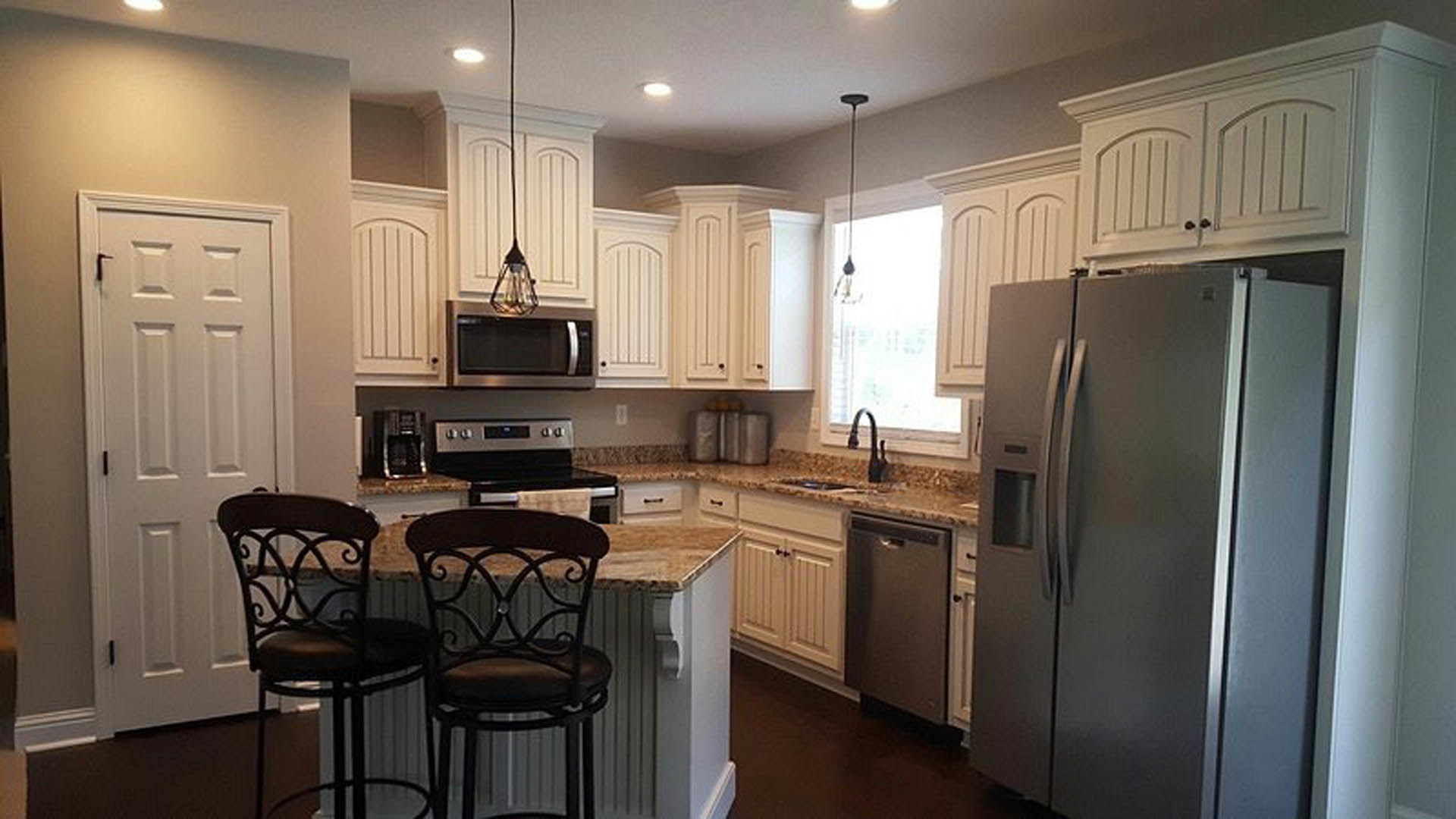 White kitchen with shaker cabinets, stainless refrigerator, bar stools with black cushions, quartz countertops, and pendant lighting over the island
