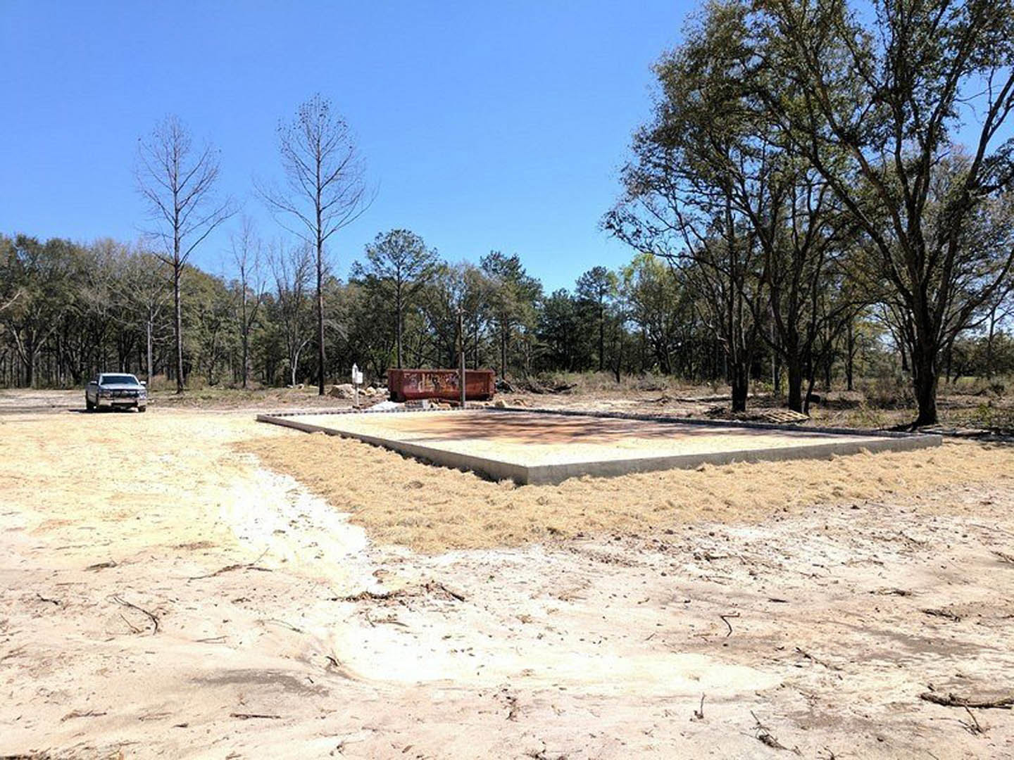 White pickup truck parked on concrete driveway in front of modern home with light-colored siding, large windows, and leafless trees in landscaped yard