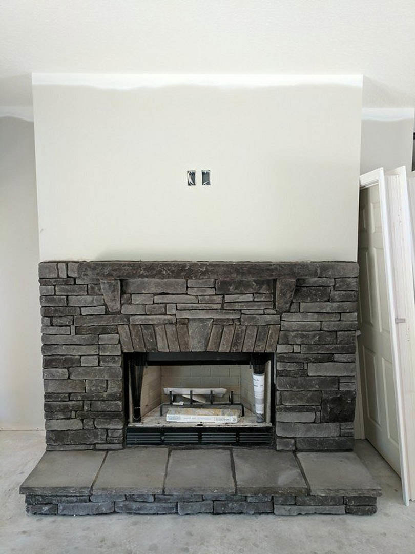 Stone fireplace with black fire screen set against a white wall, concrete floor, and adjacent white door