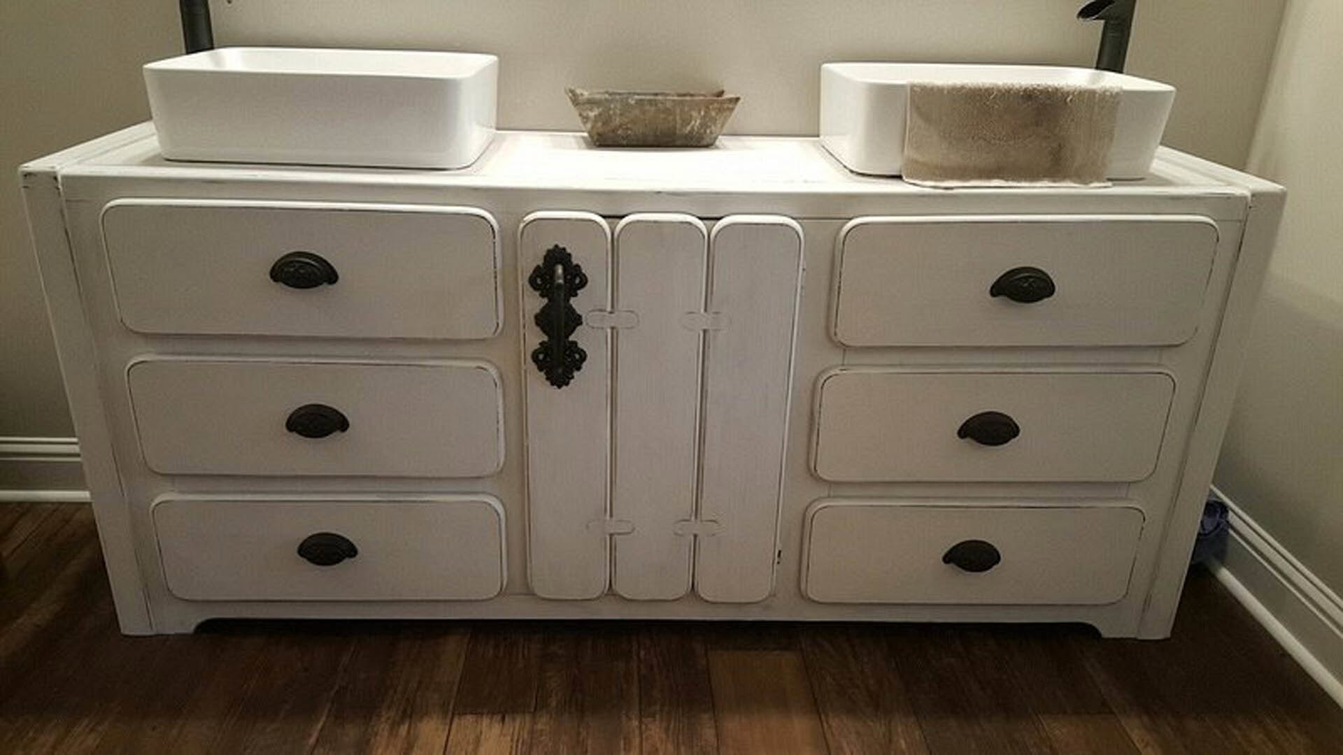 White double-sink vanity with black hardware, stone accent wall, and light fixture in a modern bathroom.