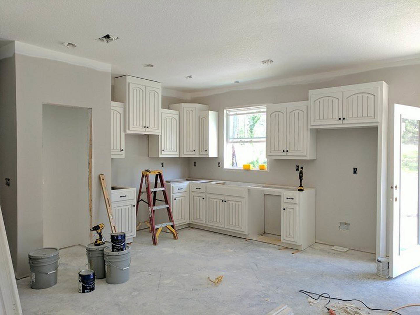 White kitchen cabinets and countertops, grey bucket with lid on floor, ladder leaning against wall, black snake on white surface, close-up of food and black can, unfinished plaster