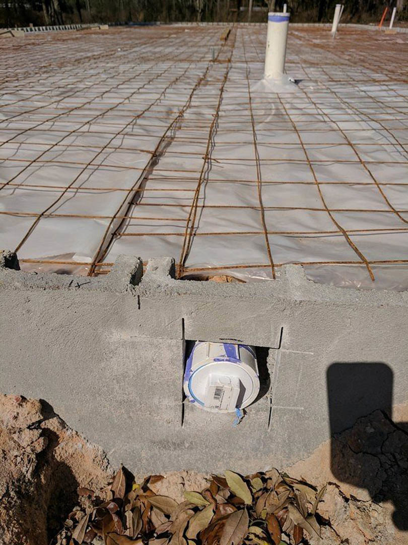 Concrete foundation with embedded metal rods, white tube, wire mesh, and scattered brown leaves on construction site