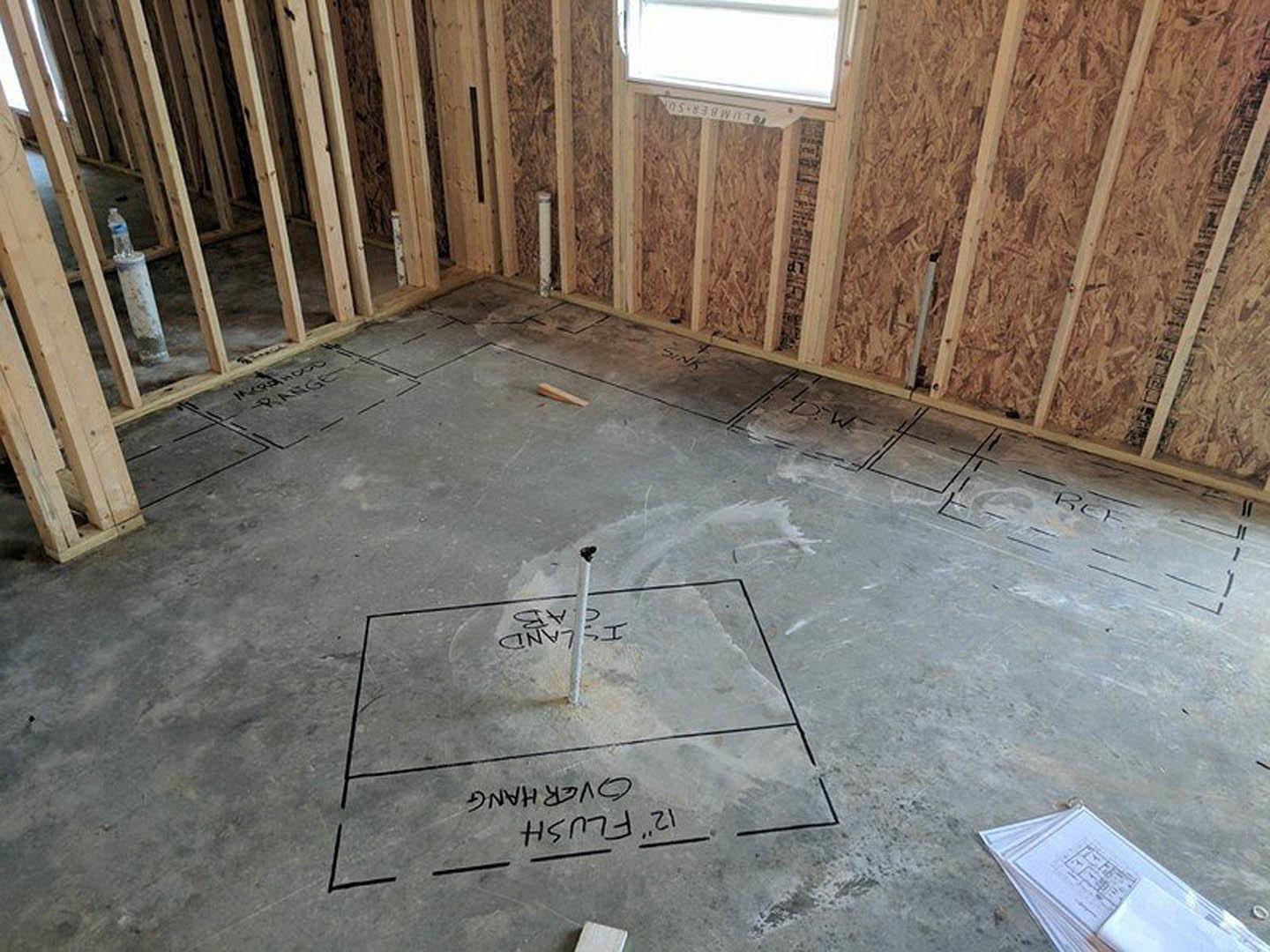 Concrete floor in a residential interior marked with construction drawings and a small hole, surrounded by building materials during remodel.