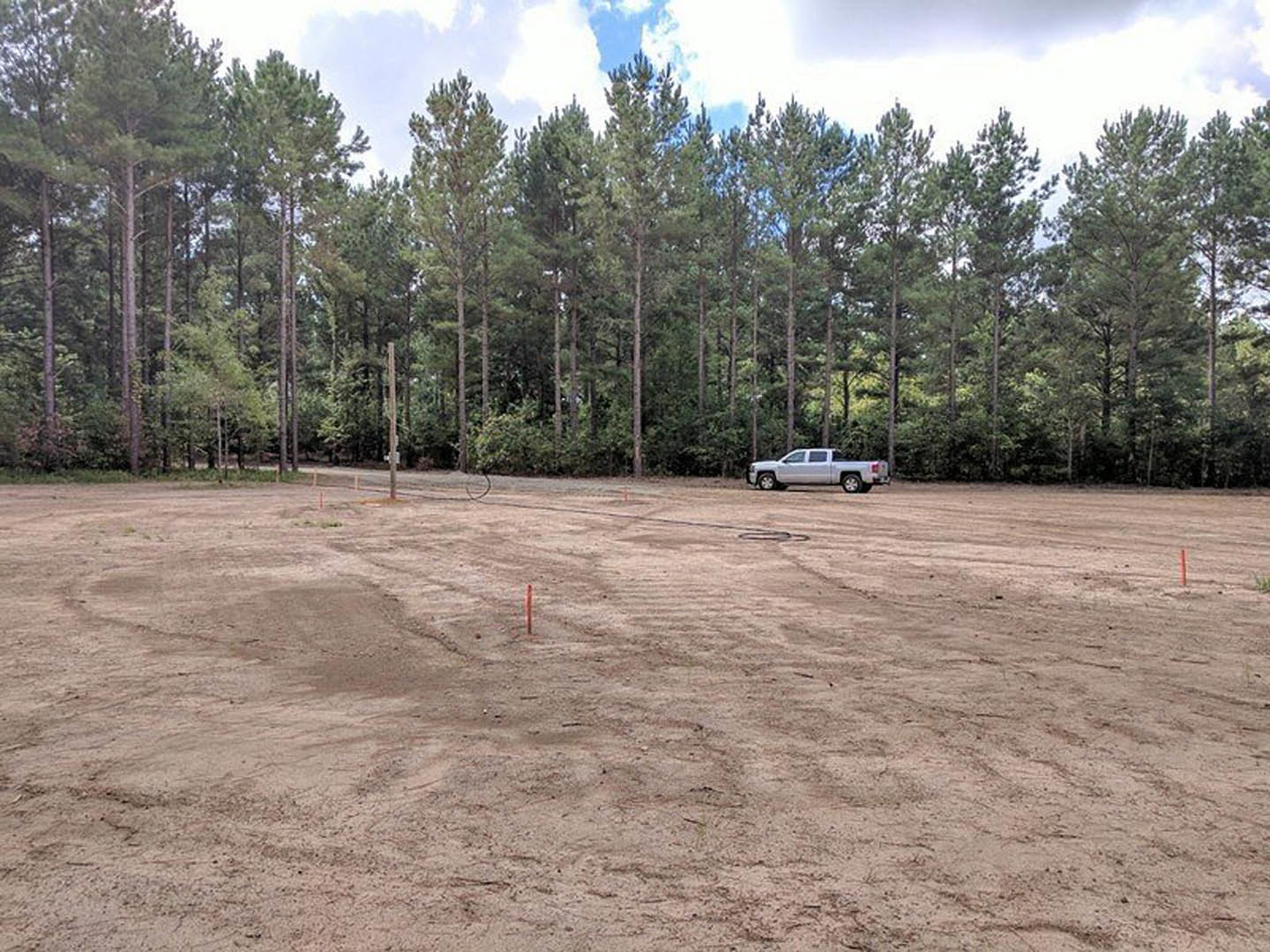 White pickup truck parked on a dirt lot surrounded by trees, blue sky with scattered clouds overhead