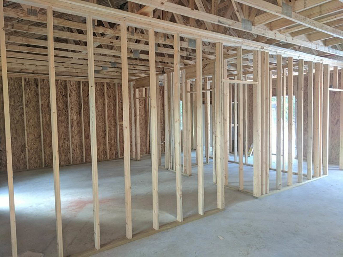 Exposed wood ceiling beams and polished concrete floor in a spacious room with unfinished wood framing and large window