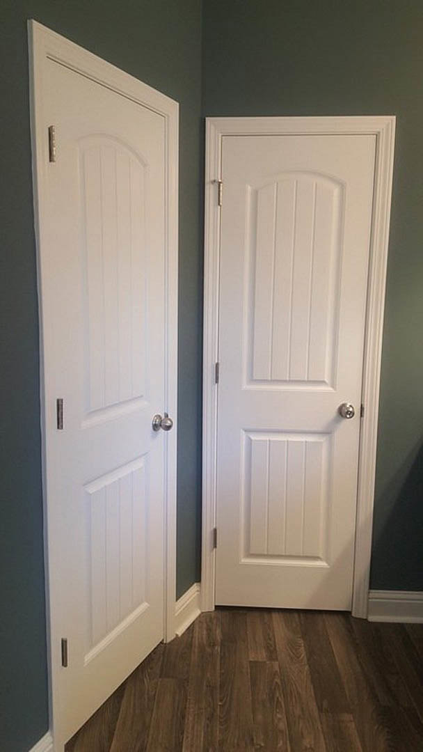 White paneled doors with silver handles set in a white wall, wood plank flooring