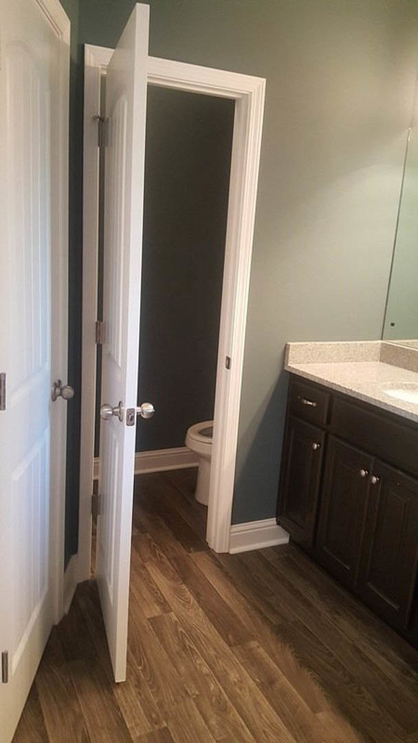 Bathroom with white toilet and rectangular sink, wood floor, white door, tile backsplash, and light wood cabinetry