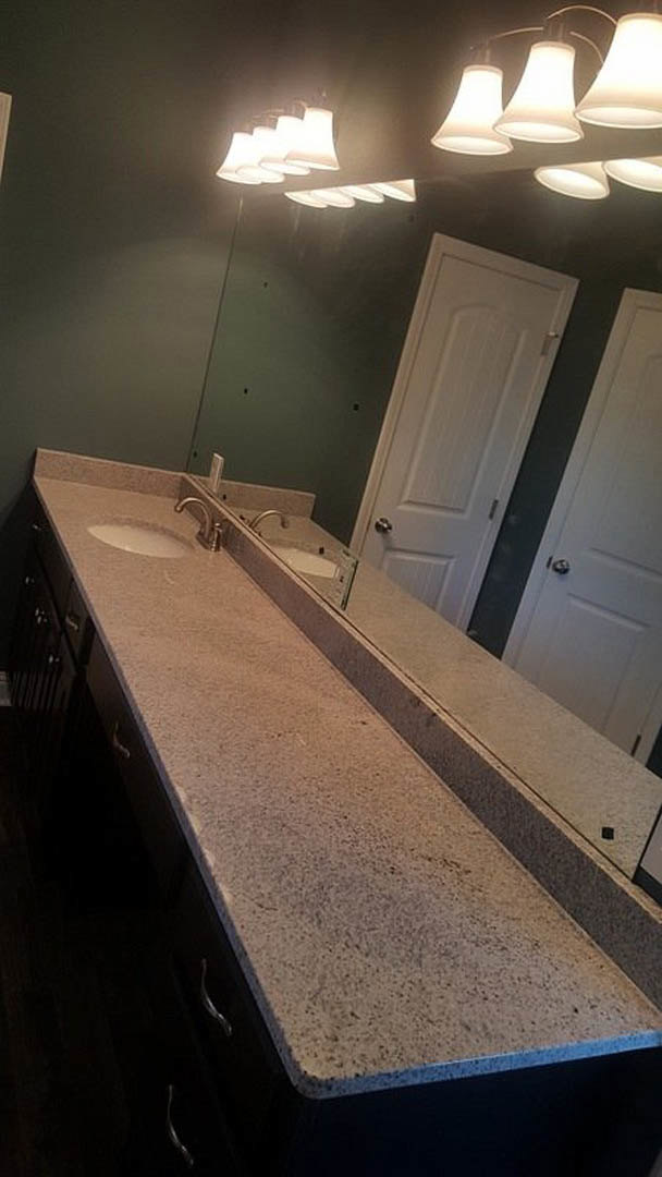 Bathroom with two undermount sinks set in a stone countertop, pendant lights hanging from ceiling, wood cabinetry below, tile flooring, and neutral wall finishes.