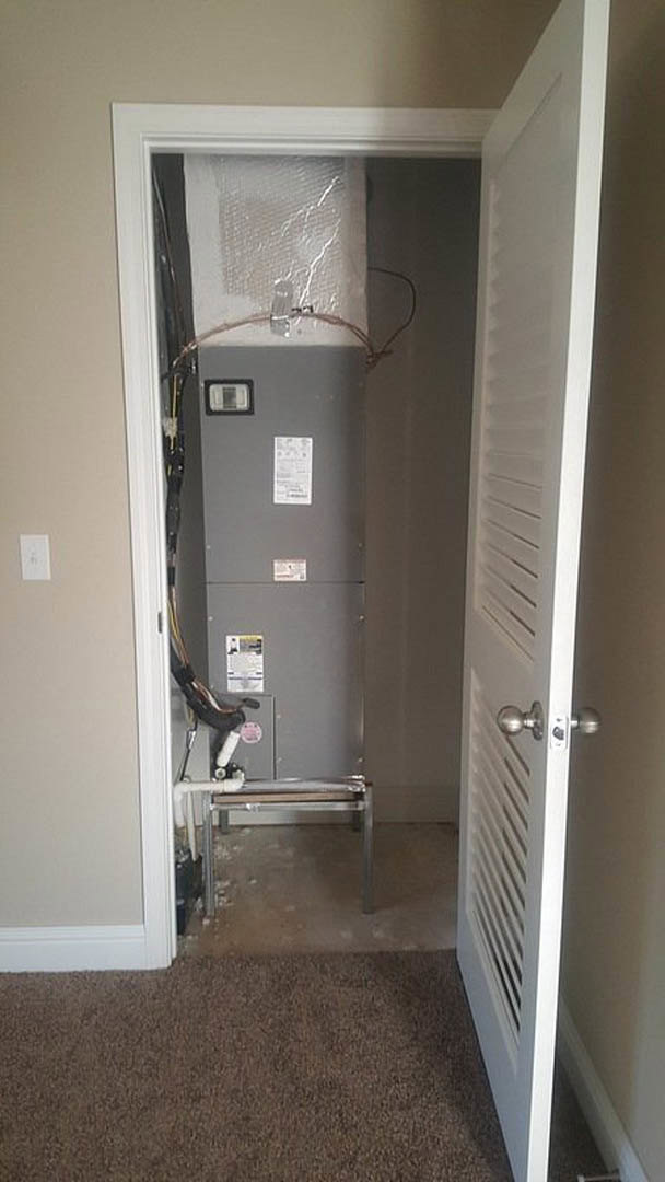 Open door revealing a room with light-colored walls, visible machine near the back, carpeted floor, table with pipe resting on the floor, close-up of metal vent and door knob, grey