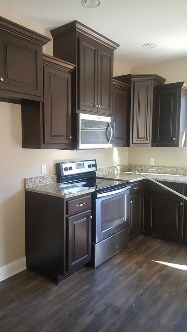 Kitchen with dark wood cabinets, stainless steel stove and oven, built-in microwave above, light stone countertops, and neutral tile backsplash