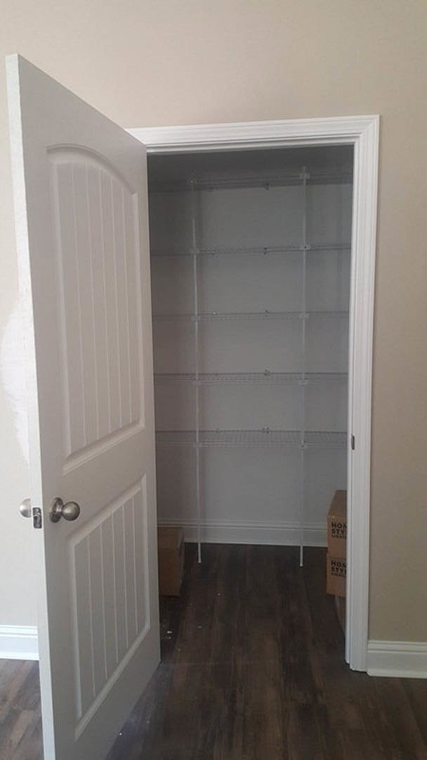 White closet with built-in shelves, open door revealing dark wood flooring and white trim