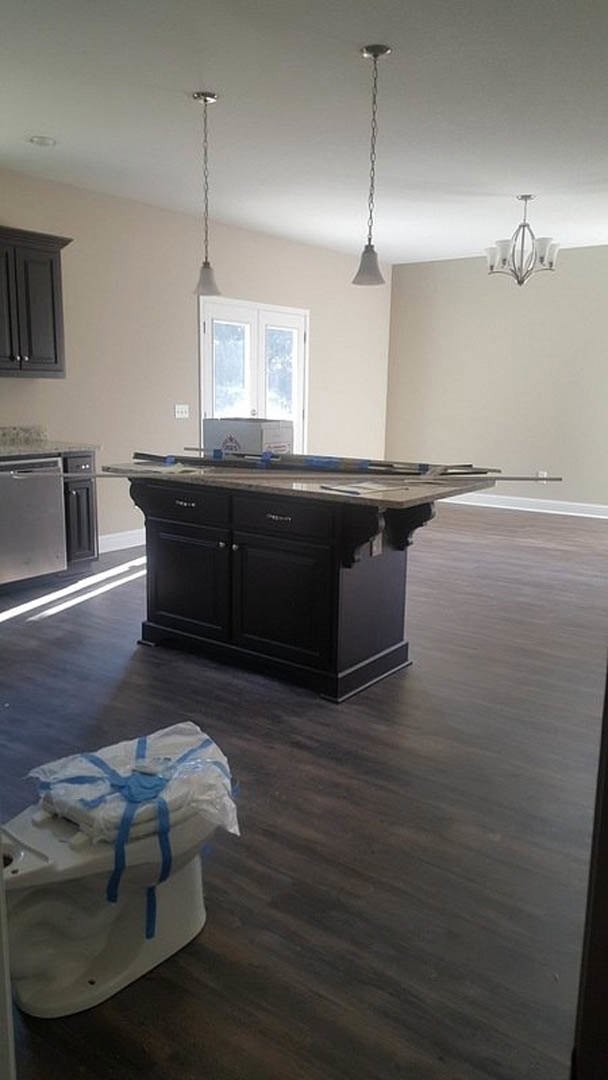 Spacious kitchen featuring a large marble-topped island, white cabinetry, stainless steel sink, wood flooring, and a glass-paneled door; miscellaneous items including a toilet with