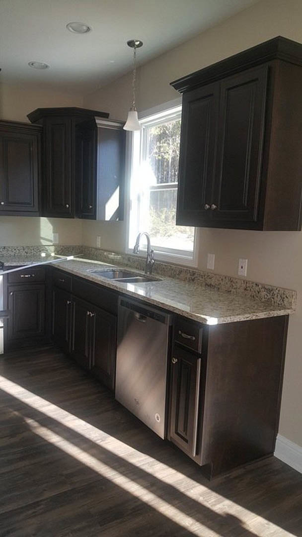Kitchen with dark wood cabinets, granite countertops, stainless steel sink, and sunlight streaming through a window onto hardwood floors