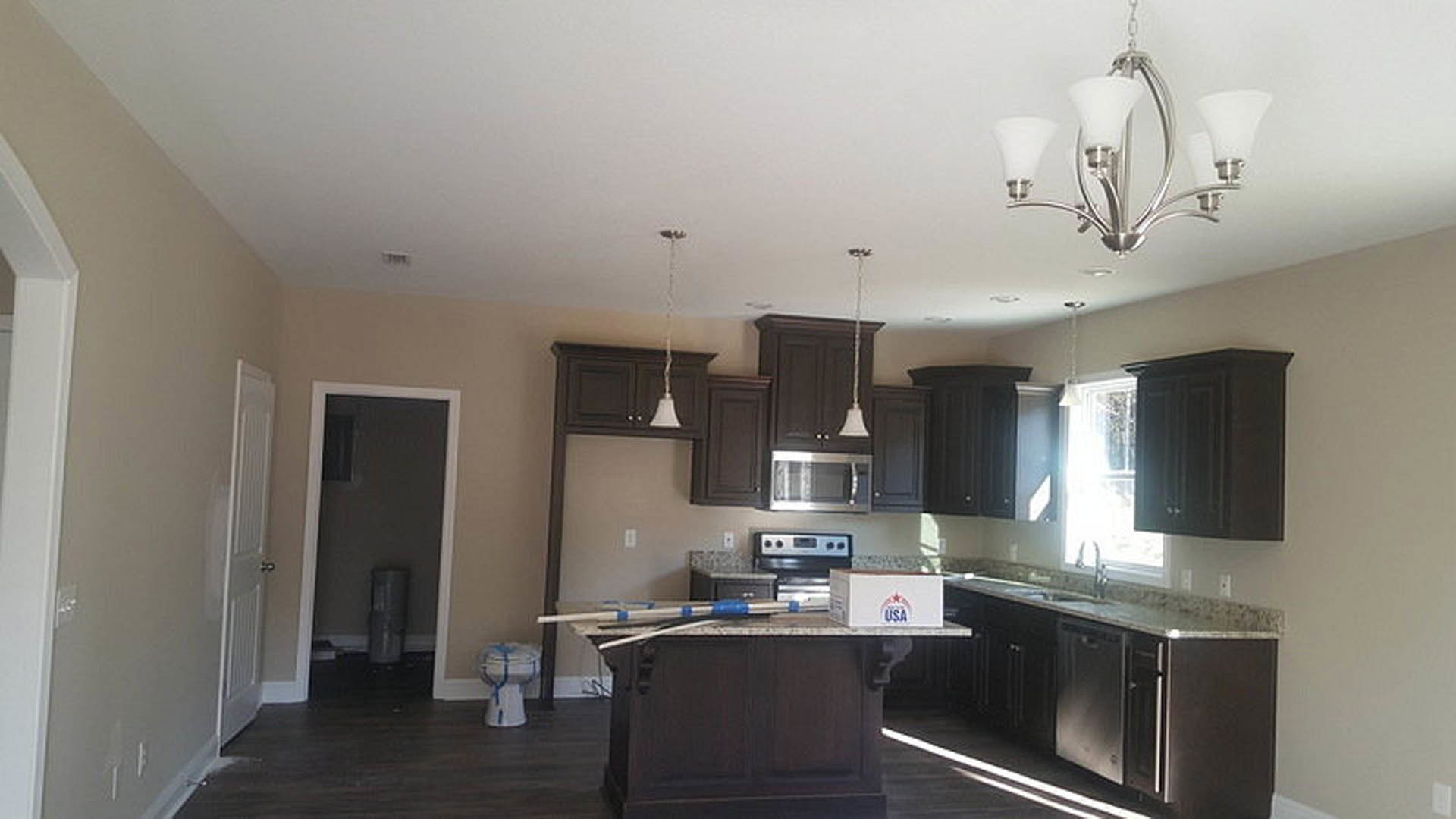 Kitchen with dark wood cabinets, light stone countertops, stainless steel appliances, and a modern chandelier above the island.