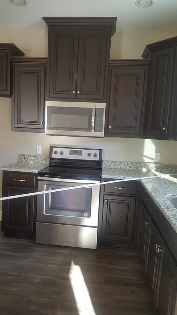 White kitchen with stainless steel stove and microwave, black cabinetry, quartz countertops, and wood flooring illuminated by recessed lighting