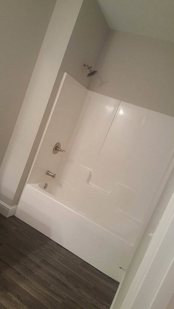 Freestanding white bathtub with chrome faucet set against light tile walls in a modern bathroom with plaster ceiling and minimal accessories