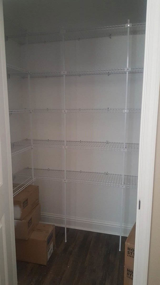Walk-in closet with built-in white shelves, stacked brown cardboard boxes, and wood flooring