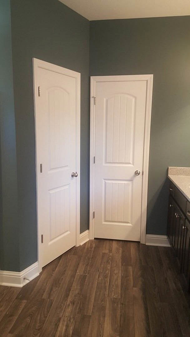 White paneled doors with silver knobs set in a room with light hardwood flooring and white baseboards, partial view of a wood railing.
