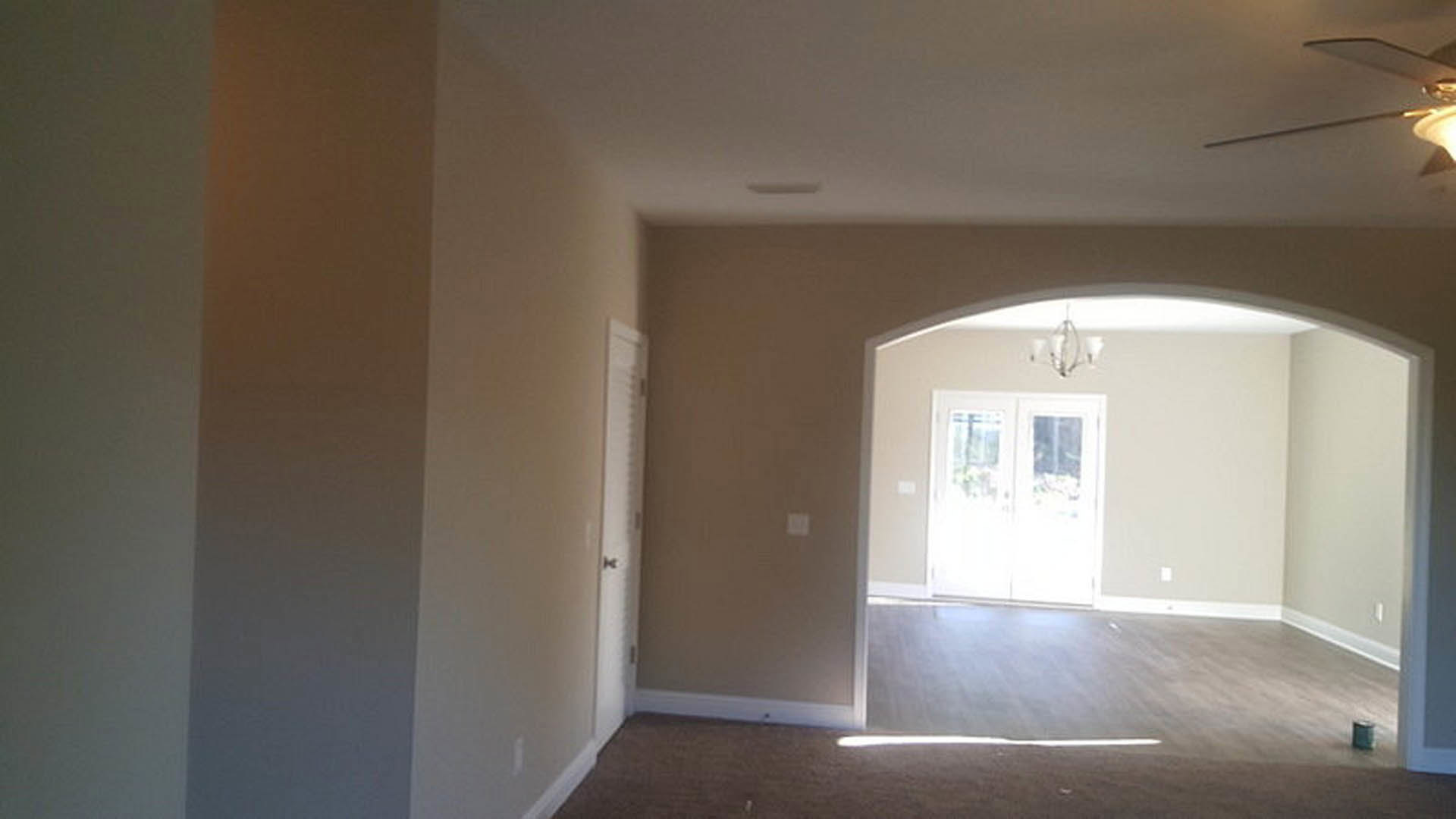Hallway with white double doors featuring glass panes, wood flooring, white walls with crown molding, and a chandelier visible in the background