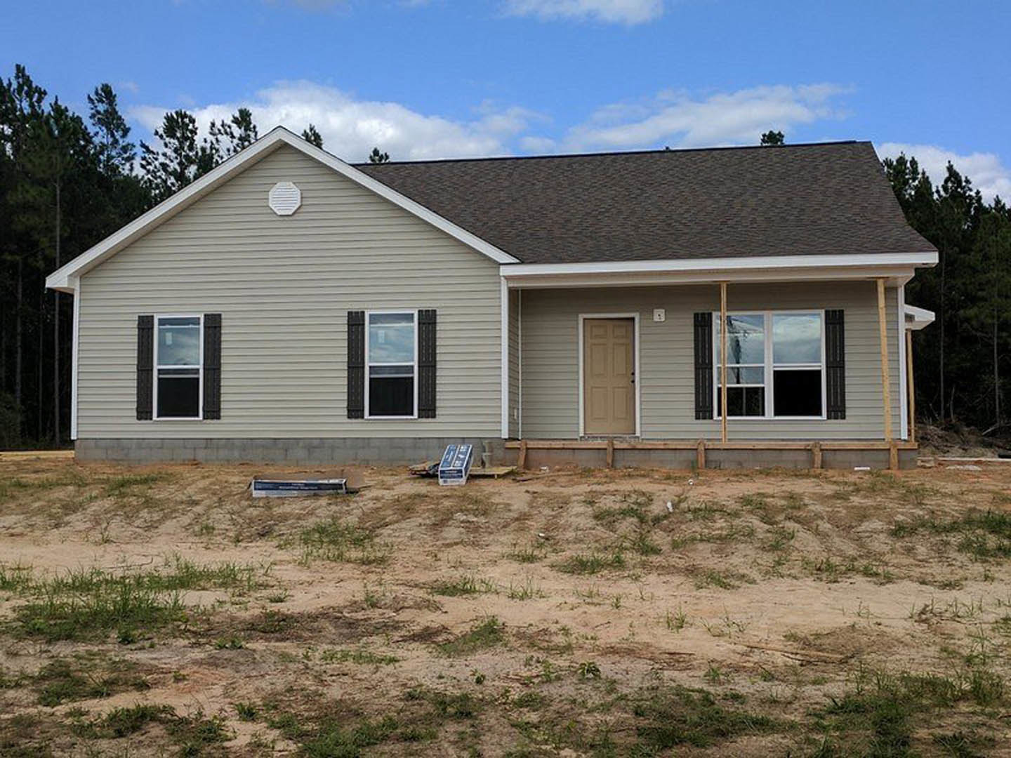 Two-story house under construction with white siding, black-framed windows, and a dirt field in front; construction sign and utility box visible near entry door.