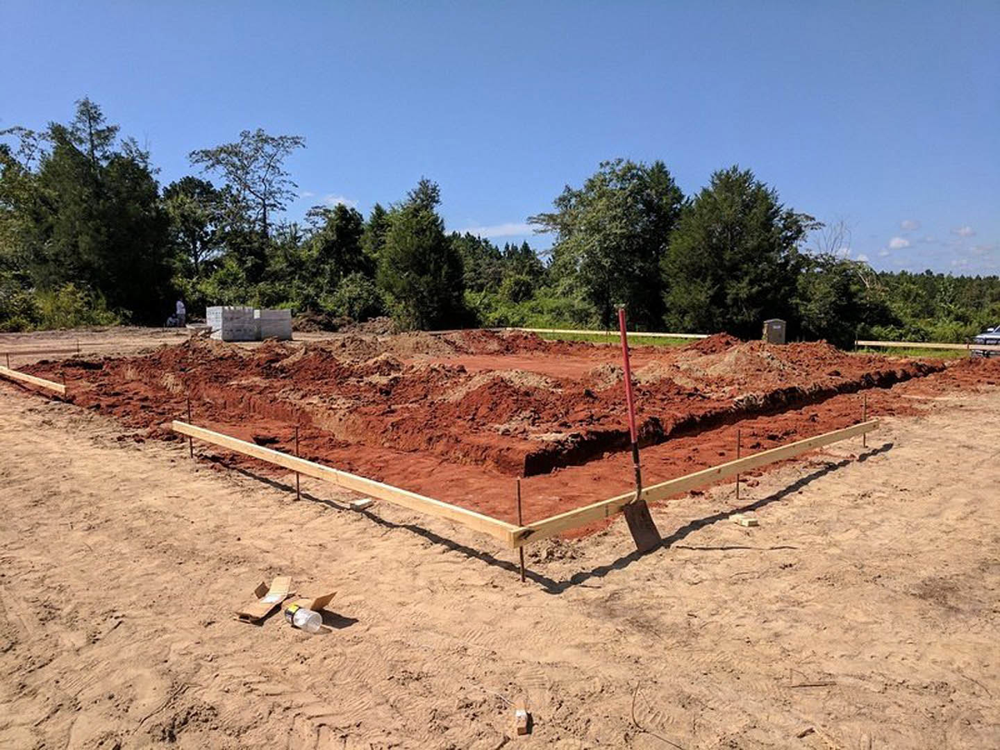 Wooden framing for a custom home under construction surrounded by dirt, scattered tools, and nearby trees