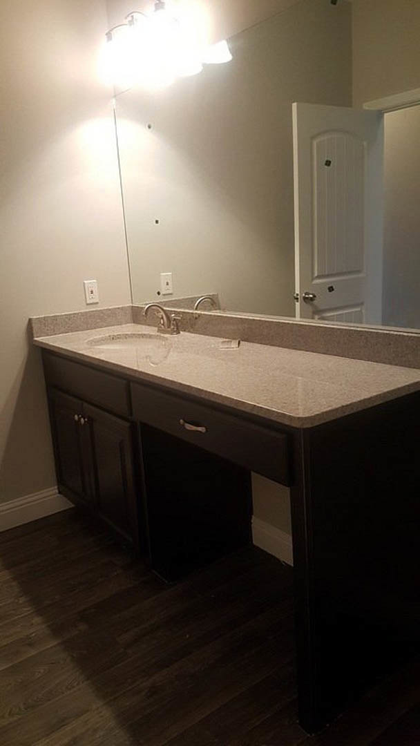 Bathroom with white tile walls, wood vanity with drawers, stone countertop, chrome faucet, and large framed mirror above sink.