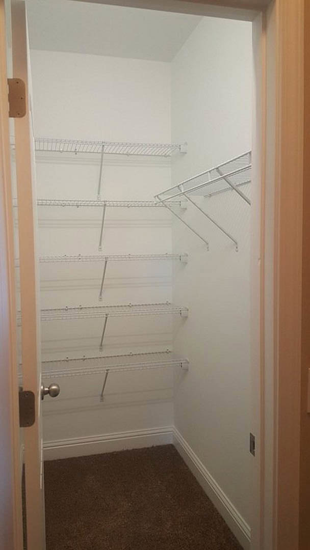 Walk-in closet with open white door, built-in metal shelving, carpeted floor, and white plaster walls