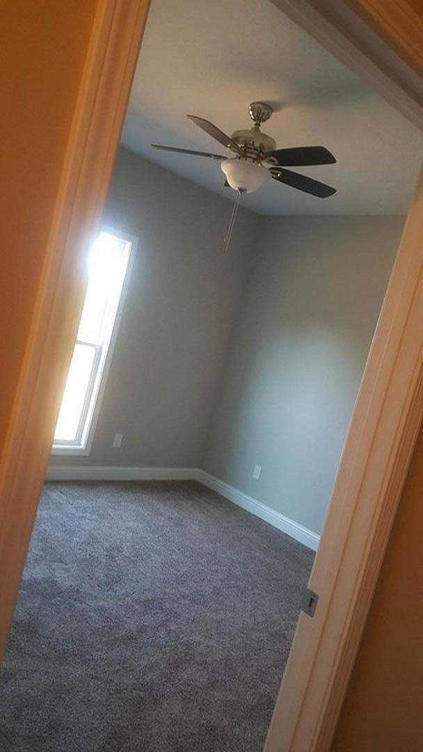 Ceiling fan with light fixture mounted above carpeted floor, open white door, neutral walls with crown molding