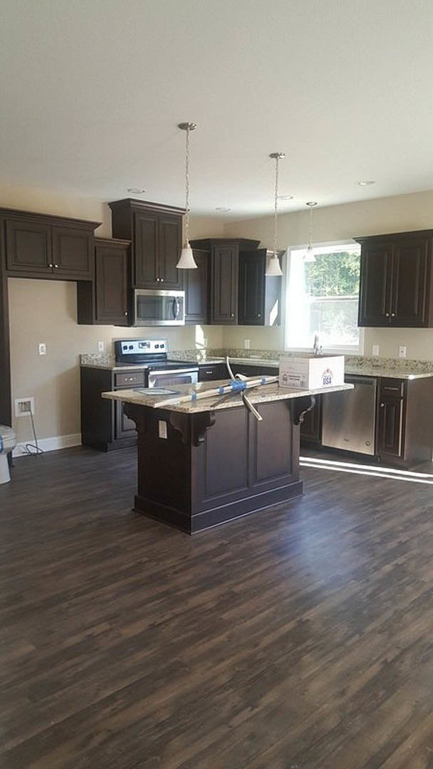 Kitchen with dark wood cabinets, large central island with black countertop, stainless steel microwave, wooden flooring, window allowing natural light, modern sink and appliances