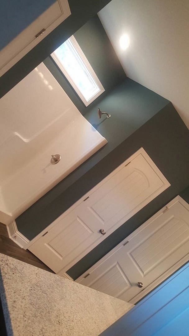 Bathroom with white cabinets and sink, freestanding white bathtub with silver drain, skylight in ceiling, white door with silver knobs, speckled white countertop