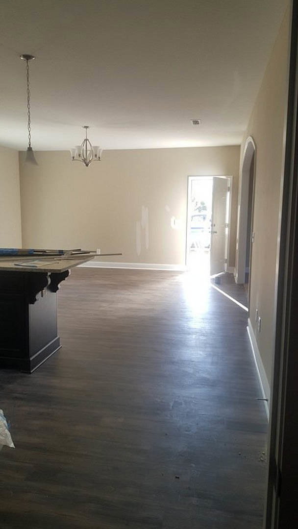 Open-concept room featuring wood laminate flooring, white walls, a kitchen island with black cabinetry, three-shade pendant light fixture, and a white door with glass panels.