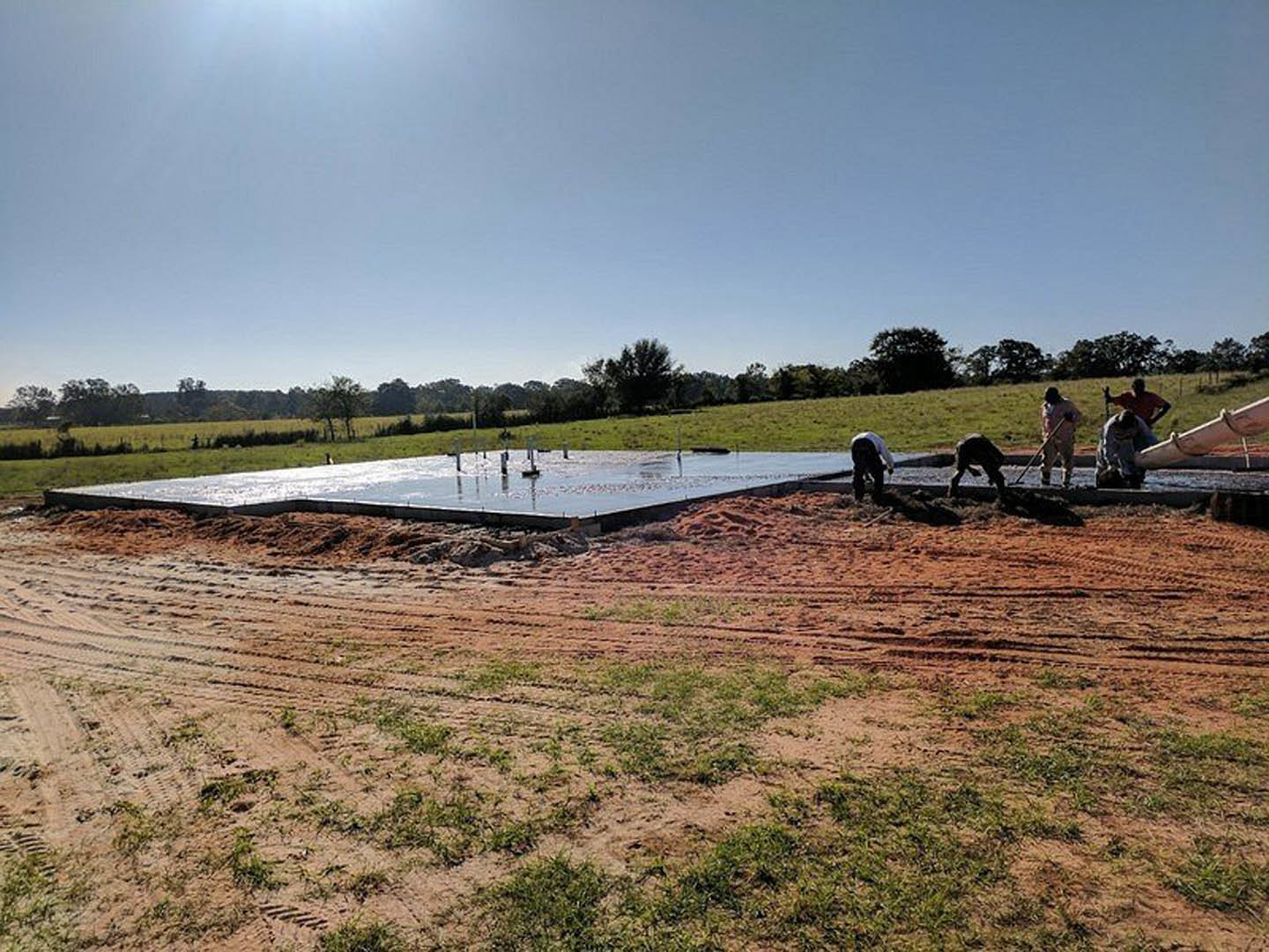 Modern farmhouse with white siding and black-framed windows, surrounded by a grassy field and mature trees under a clear sky
