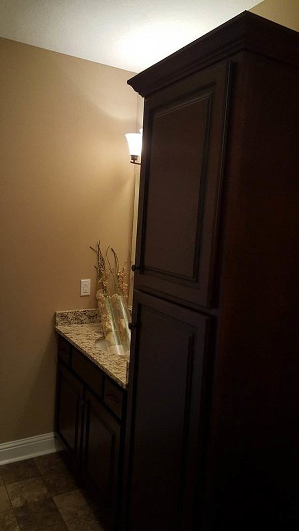 Marble countertop with undermount sink, brown tile floor, white baseboard, cabinetry, and partially visible curtain in custom bathroom