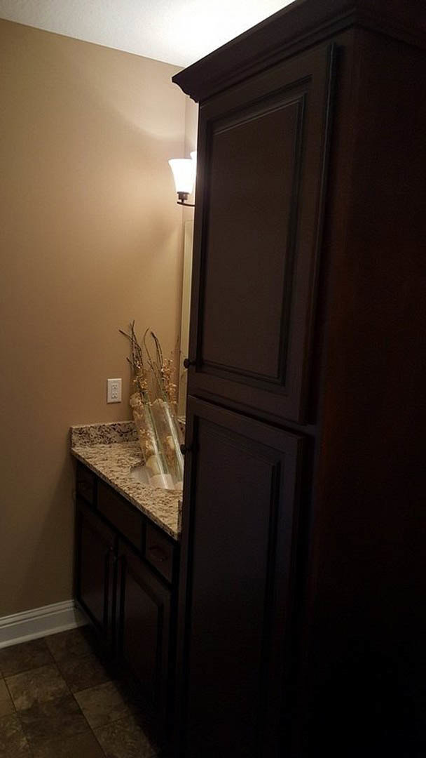 Modern bathroom featuring light wood cabinetry, sleek drawers, and a contemporary wall-mounted light fixture; decorative vase and glass sit atop the vanity against neutral walls