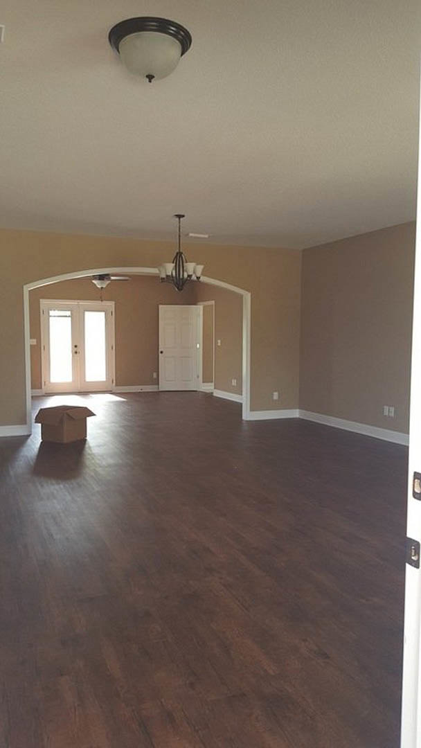 Bright room with hardwood flooring, white plaster walls, white double doors with glass panels, ceiling light fixture, and a brown cardboard box placed near the center