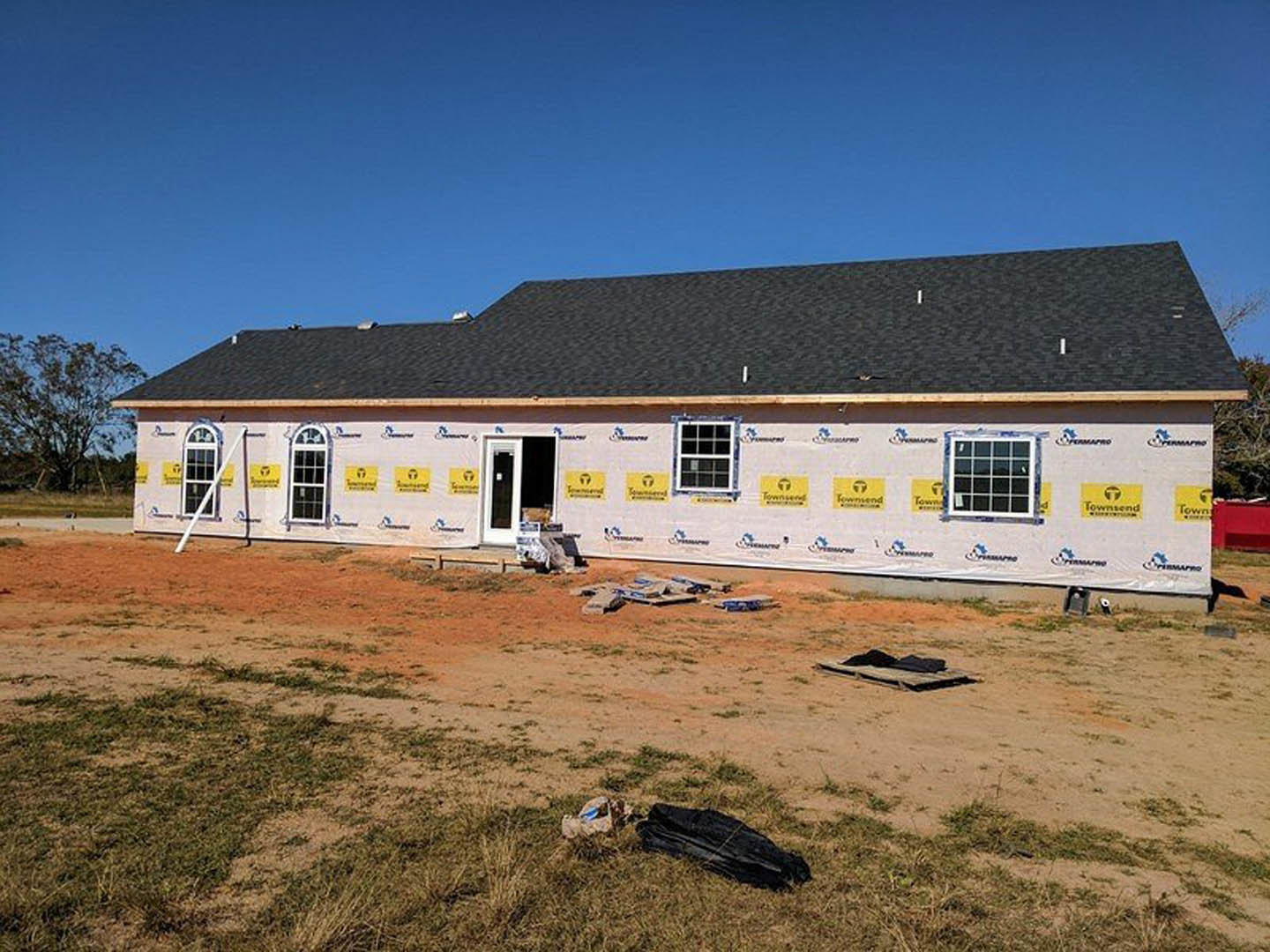 Partially built house with white door and black screen, yellow construction signs, leafless tree, scattered construction materials, multi-pane window, and black object on ground in