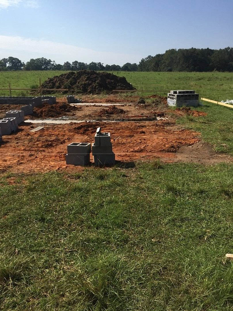 Brick pile and concrete blocks on grassy construction site under blue sky with scattered clouds.