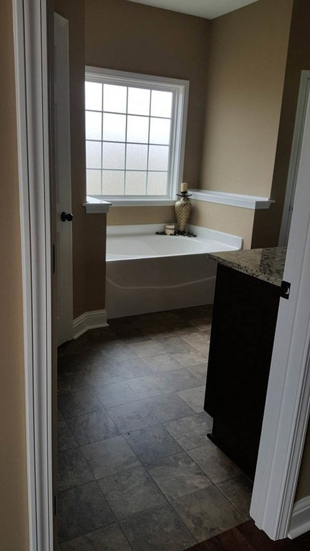 Bathtub beside marble countertop, grey tile floor, black door, large window, chrome plumbing fixtures