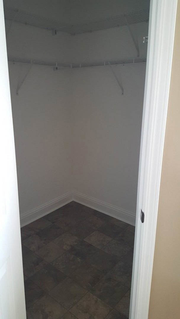 Closet with white plaster walls, grey tile flooring, white door frame, and black grout line along the floor