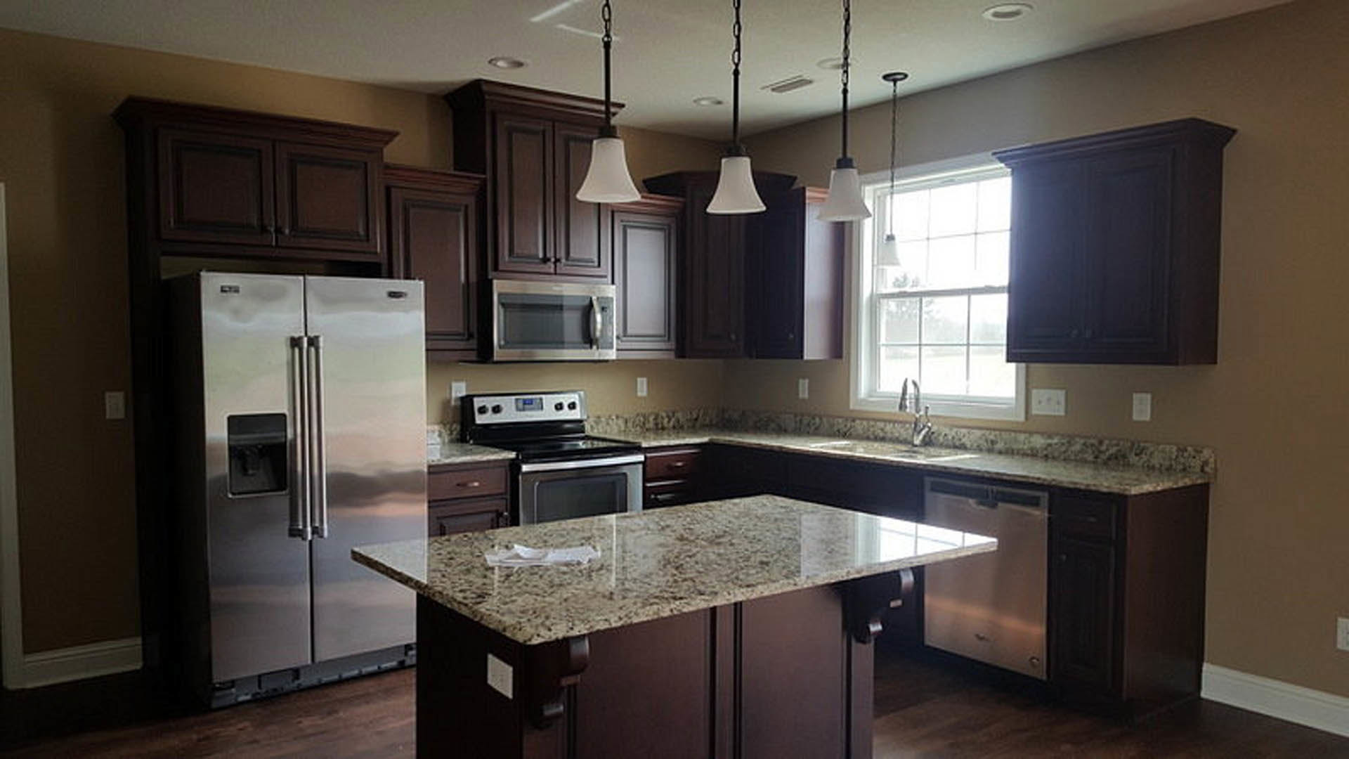 Granite countertops, stainless steel refrigerator and stove, white cabinetry, marbled surface, modern sink, under-cabinet lighting, blurred person in black shirt near appliances