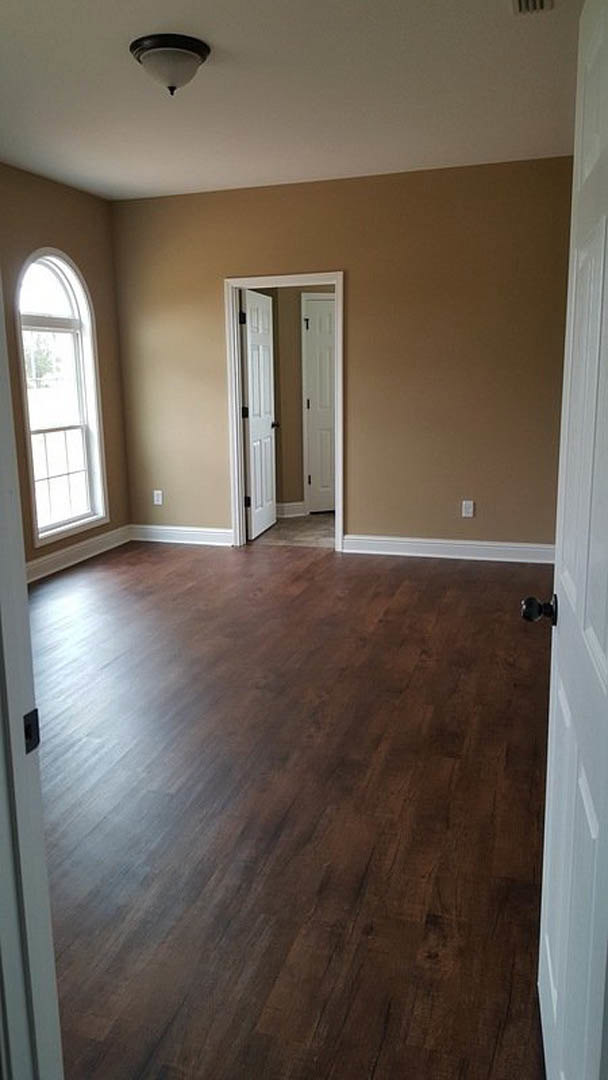 Hardwood floor in a room with white walls, white-framed window, white door, and ceiling light fixture
