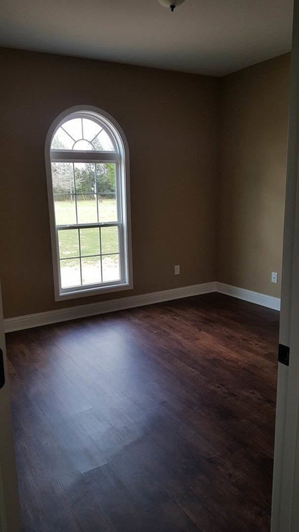 Dark wood floor in a room with a large window overlooking a grassy field, white walls, and a ceiling light fixture