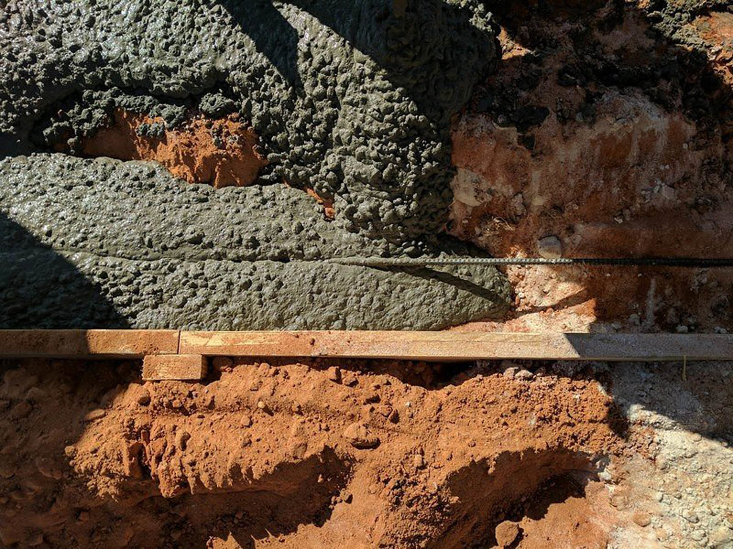 Smooth concrete slab resting on compacted dirt, surrounded by exposed soil and scattered rocks in an outdoor construction area