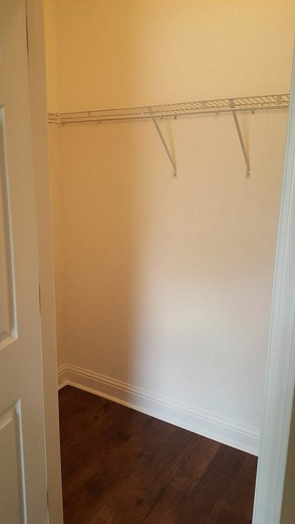 Closet with wood flooring, white plaster walls, two white metal shelves, and metal rods for hanging clothes