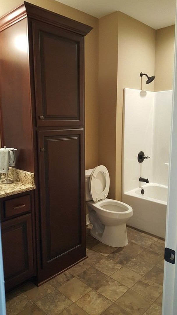 White-tiled bathroom featuring a bathtub, toilet with seat up, wall-mounted mirror, and chrome fixtures